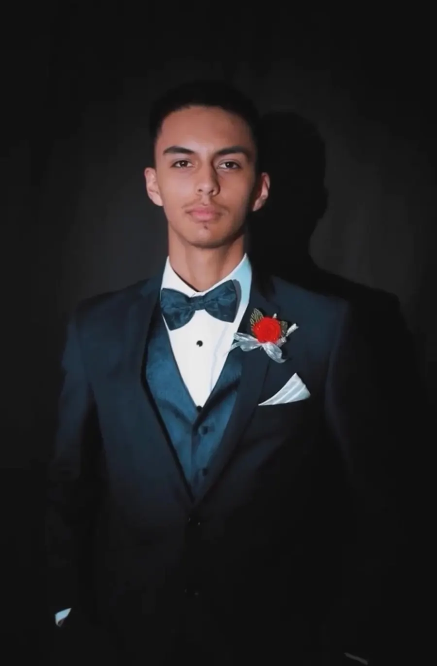 A Royal Tuxedos customer in a navy tuxedo with a red boutonniere, photographed for prom