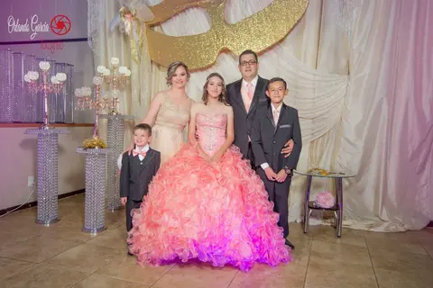 A quinceañera in a pink gown with her family in matching suits